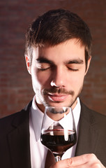 Man sniffing red wine in glass on brick wall background