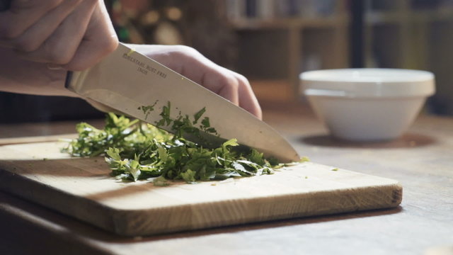 	A chef chops parsley on the kitchen board, pan, close up