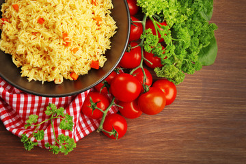 Stewed rice with a carrot on a black plate over wooden background