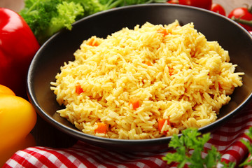 Stewed rice with a carrot on a black plate, close up