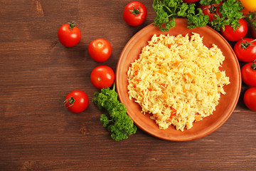 Stewed rice with a carrot on a brown plate over wooden background