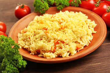 Stewed rice with a carrot on a brown plate over wooden background, close up