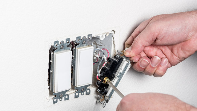 Electrician replaces a light switch in a white wall