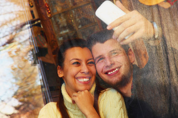 Young happy coupletaking selfie at cafe, view through a window