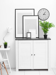 Room interior with commode, lamp, frames and clock on white wall background