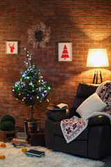 Living room interior with black armchair, lamp and Christmas tree on brick wall background