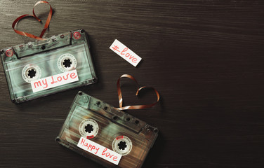 Retro audio cassettes with tapes in shape of hearts on wooden background