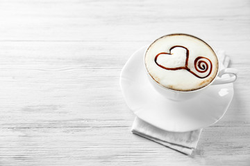 Cup of cappuccino with chocolate syrup on light wooden table
