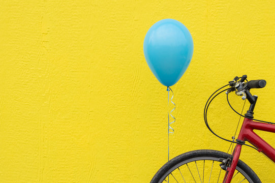 Red bike with a blue balloon against a bright yellow wall.