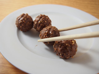 Taking by chopsticks, milk chocolate balls with almond and peanuts on white dish