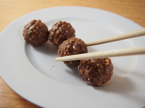 Taking By Chopsticks, Milk Chocolate Balls With Almond And Peanuts On White Dish