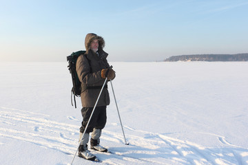 The traveller's portrait with a beard and ski sticks against snow and the blue sky
