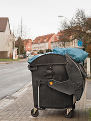 Blaue Müllsäcke gucken aus einem offenen fahrbarem Müllcontainer