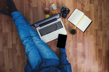 Man working on a wooden floor with his laptop, phone, tablet and agenda.