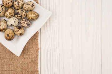 Fresh quail eggs in a white plate on a wooden background