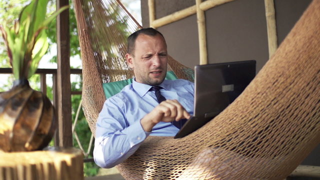 Angry businessman destroying laptop while lying on the hammock on terrace, 240fps
