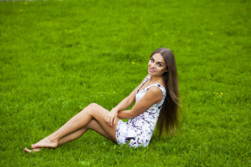 Sexy woman in short dress sitting on green grass