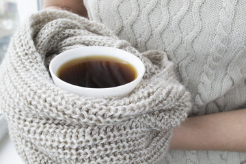 Coffee cup in female hands with a scarf
