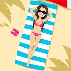 Beautiful brunette woman wearing pink bikini lying on the beach on a white and blue striped towel