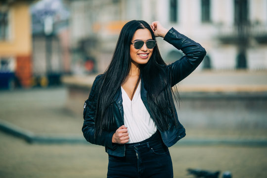 Young fashion brunette woman in sunglasses with jacket on city street