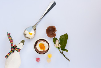 Cholocate Easter egg next to spoon with yolk, eggshell and candy