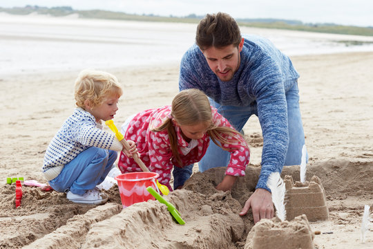 Father And Children Building Sandcastles On Beach Together