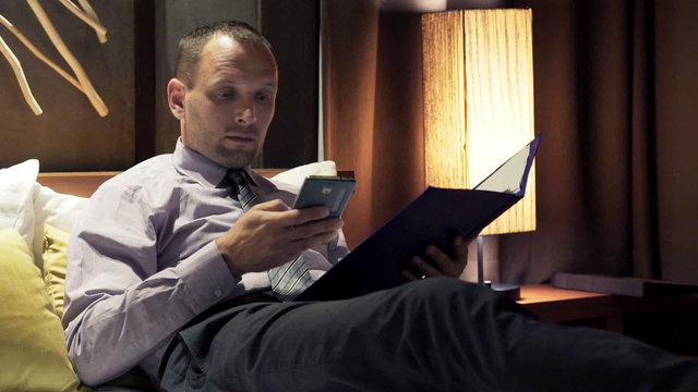 Businessman working with documents and smartphone sitting on sofa at home

