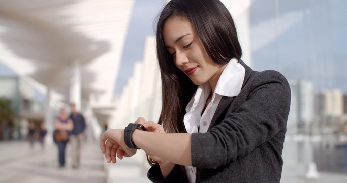 Attractive woman checking the time on her wristwatch as she sits on a bench in town waiting for a rendezvous