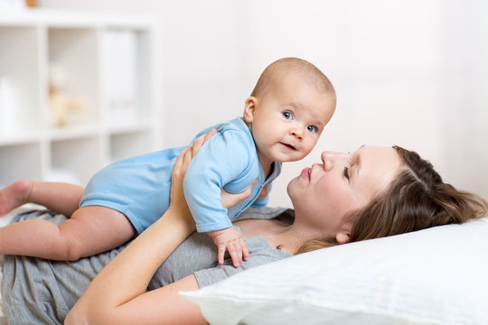 Mother and baby laugh and play lying on bed