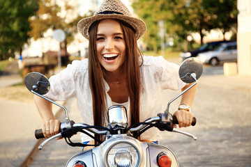 Portrait of a beautiful girl sitting on silver retro scooter, smiling and looking at the camera