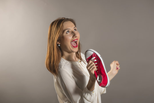 Cheerful attractive teen girl sing song holding a red shoe like a microphone holding it near her face, studio shot against gray background