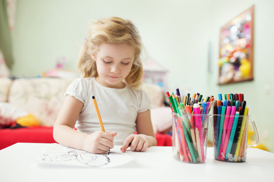 Portrait of child blonde girl drawing at home in her room