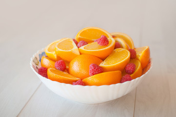 A large plate of sliced oranges and raspberries on white table.