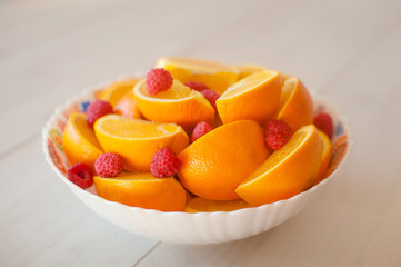 A large plate of sliced oranges and raspberries on white table.