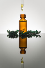 Essential oil with thyme leaves, in amber glass bottle with dropper, vertical with reflection - 102817578