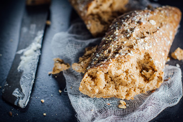 Torn baguette from dark bread with seeds .and a knife smeared with butter.