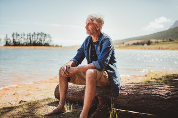 Fototapeta premium Mature man sitting on a log near lake