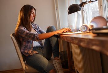 Young female blogger working at home.She sitting in her working room and typing something on laptop.