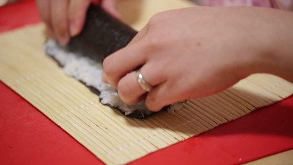 A woman prepares sushi rolls with a bamboo mat