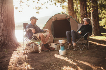 Couple relaxing on chairs by tent at campsite