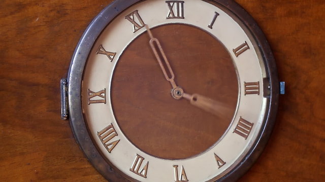 Close up view of vintage wooden clock with roman numerals and hands rotating
