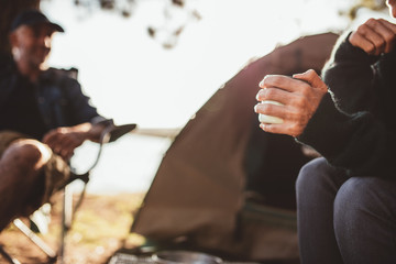 Hand of a woman holding coffee at campsite - obrazy, fototapety, plakaty