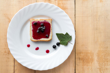 Bread with jam and drops in white plate on wooden table.