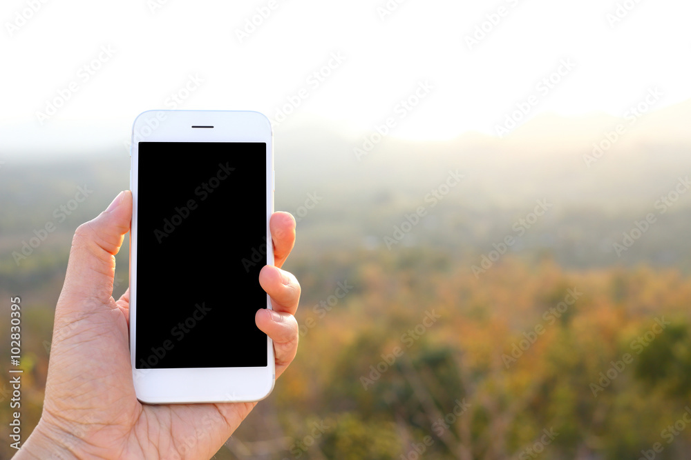 Wall mural hand holding mockup smartphone with sunlight and mountain backgr