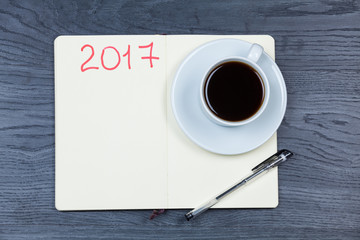 2017 planning agenda. Book with cup of coffee on wood background.