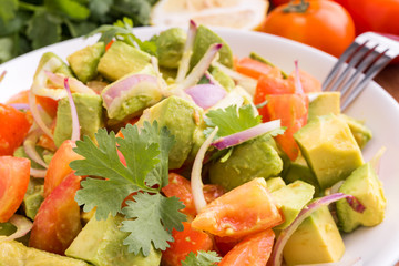 Fresh avocado Salad  with tomatoes, purple onion on the white dish. Healthyt food concept