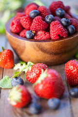Raspberries, strawberry and blueberry on a wooden board. Natural background. Selective focus.