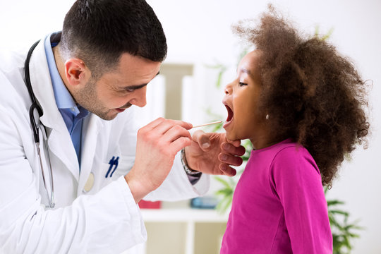 Pediatrician examining cute smiling african girl, throat sick