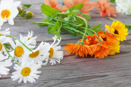 Chamomile, calendula and other garden flowers for a bouquet on a wooden table in the background of a summer garden