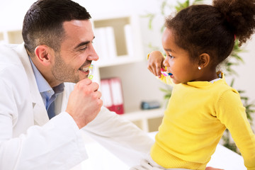 Specialist pediatrician shows to child how to brush teeth